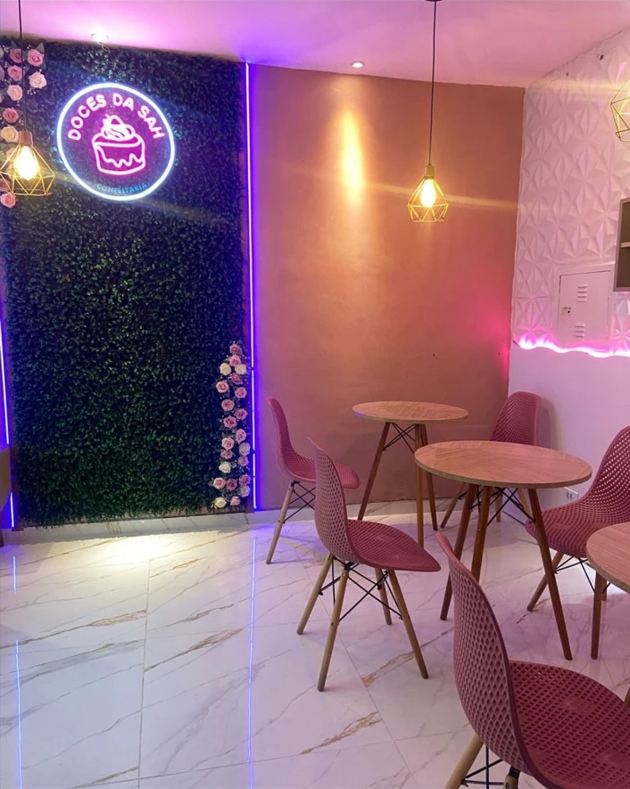 Interior da Doces da Sah com mesas, cadeiras rosas e letreiro da confeitaria